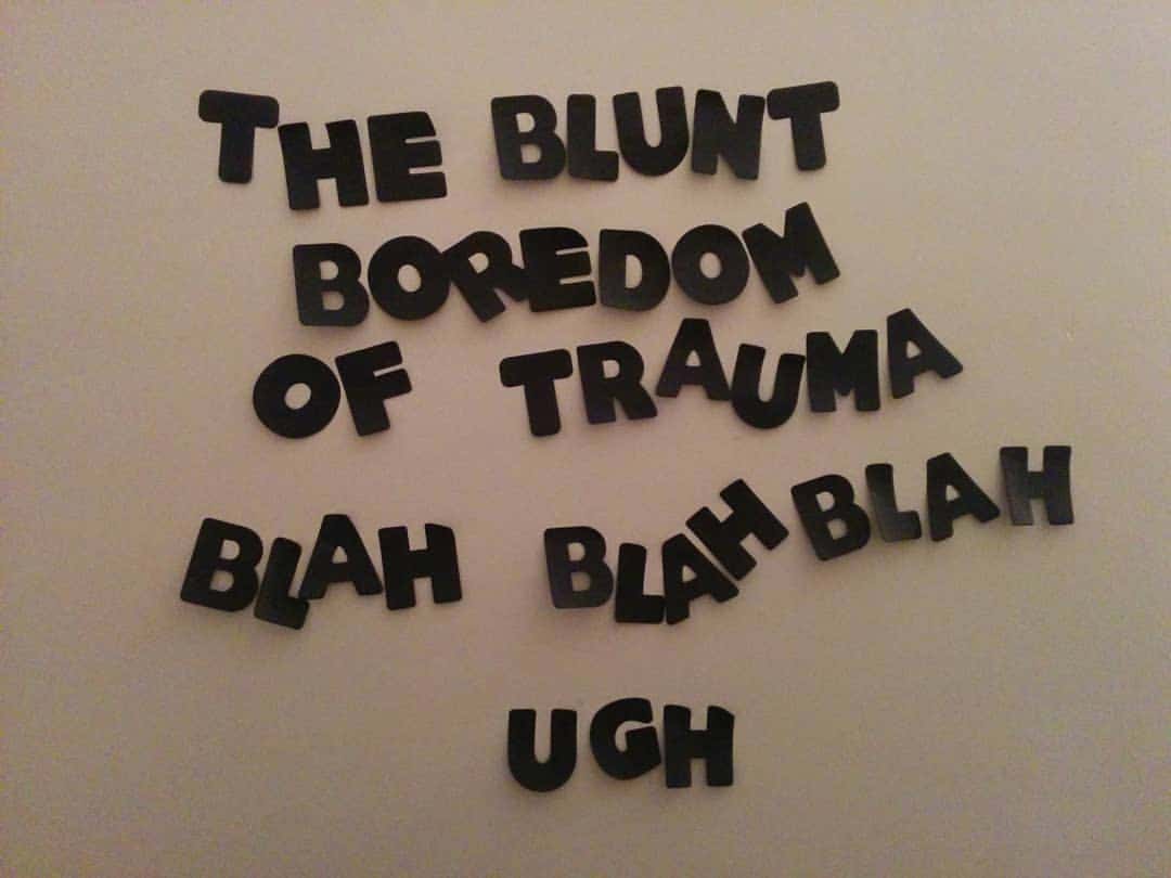 paper letters stuck to a blank wall that read "THE BLUNT BOREDOM OF TRAUMA. BLAH BLAH BLAH. UGH."