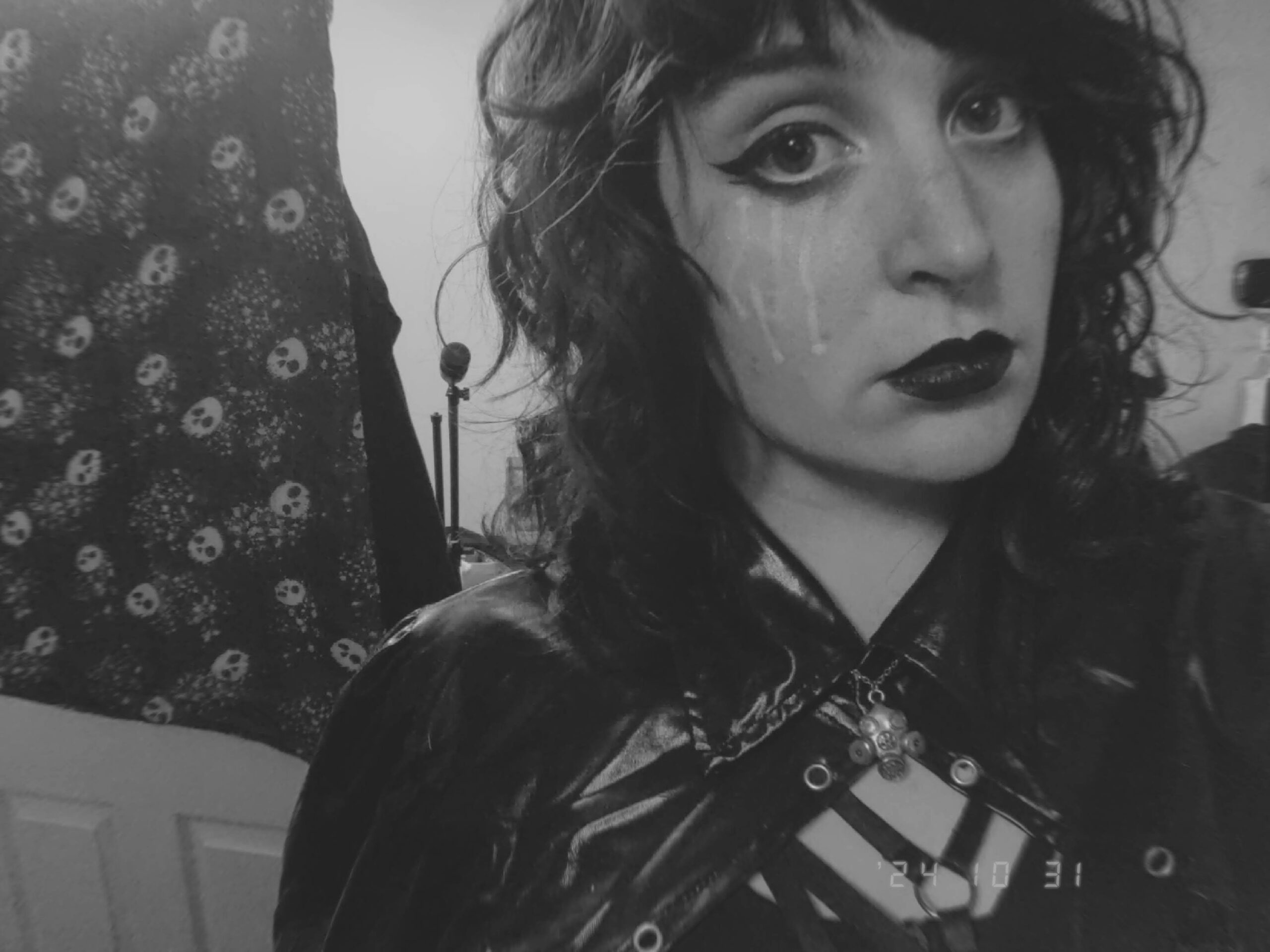 a greyscale picture of me, a white femme with shoulder-length curly dark hair, winged eyeliner, & black lipstick